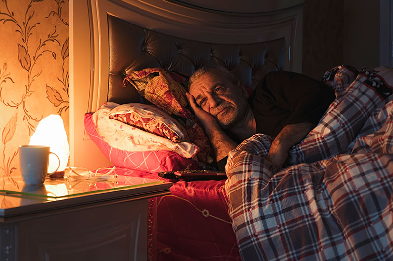 A man lies in bed awake because sleep patterns in older adults can change. 